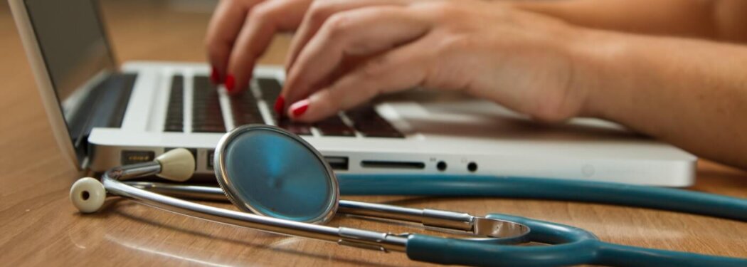 person sitting while using laptop computer and green stethoscope near