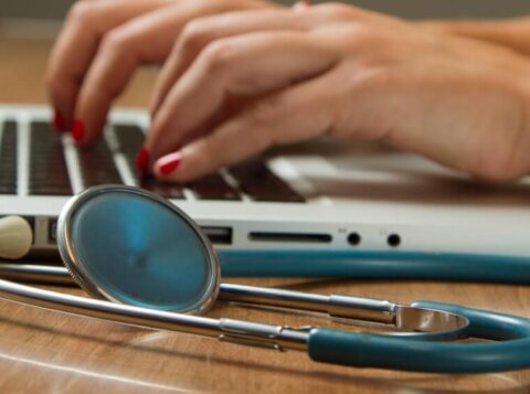 person sitting while using laptop computer and green stethoscope near