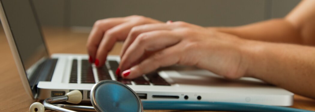 person sitting while using laptop computer and green stethoscope near