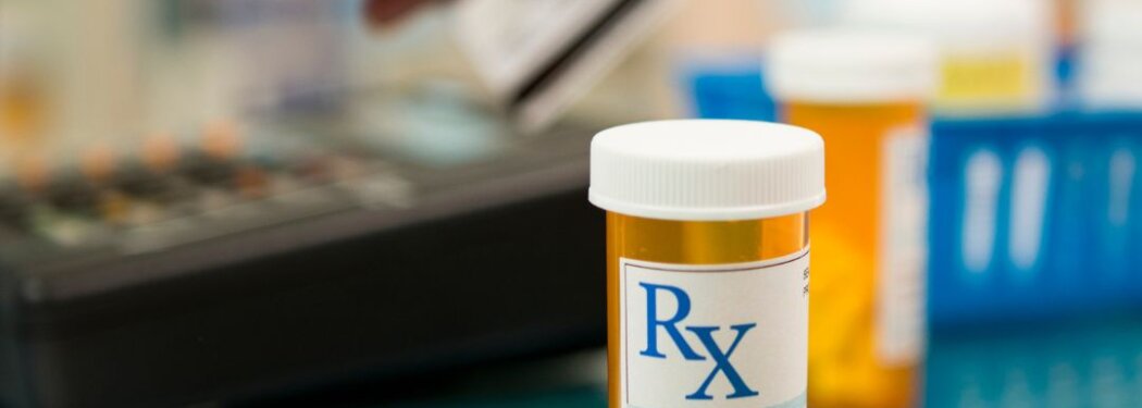 A prescription container pictured in front of someone's hand swiping a credit card