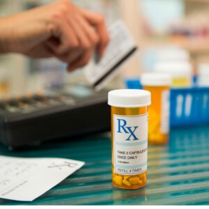 A prescription container pictured in front of someone's hand swiping a credit card